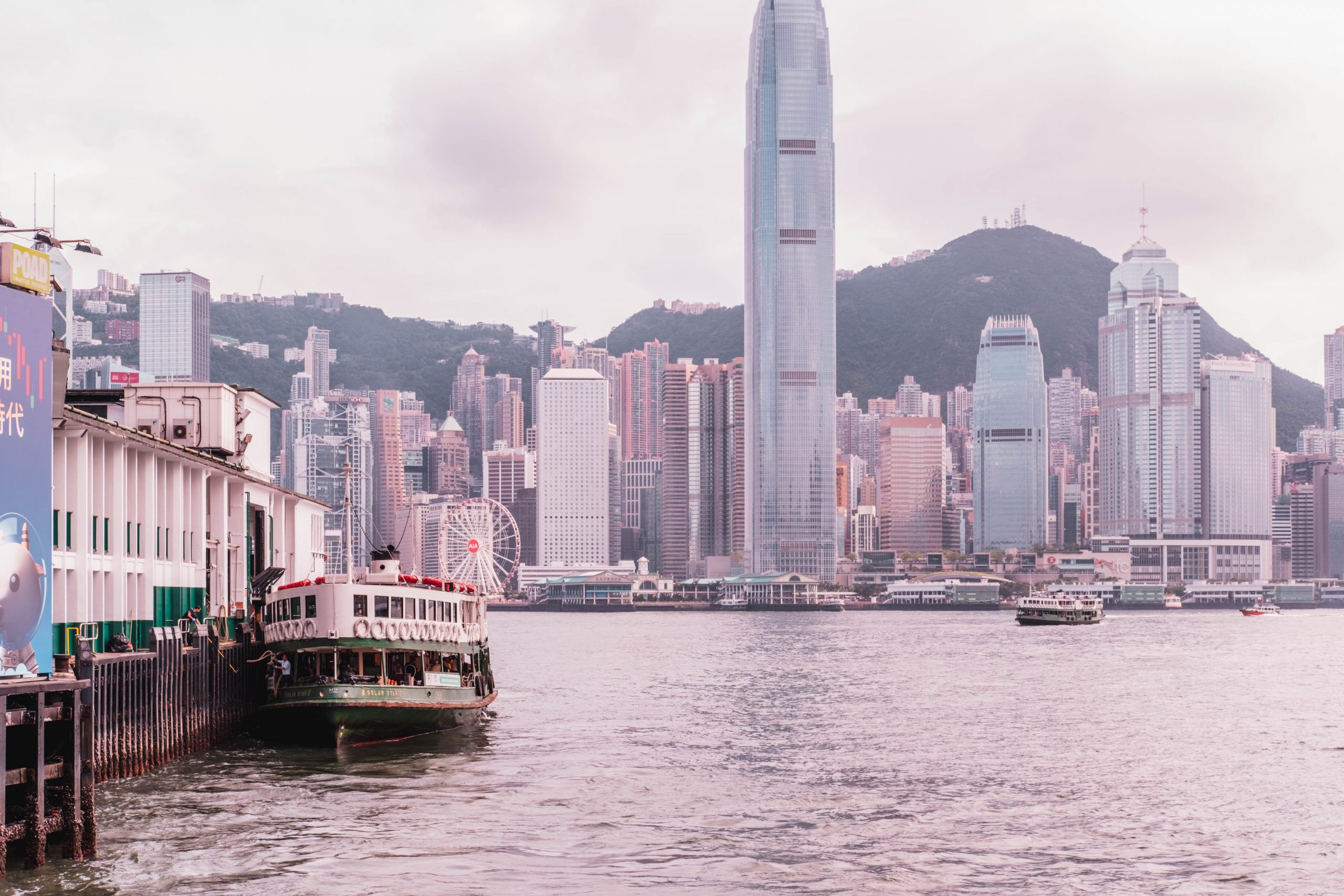 Ferry on water with city skyline and mountains in the background.